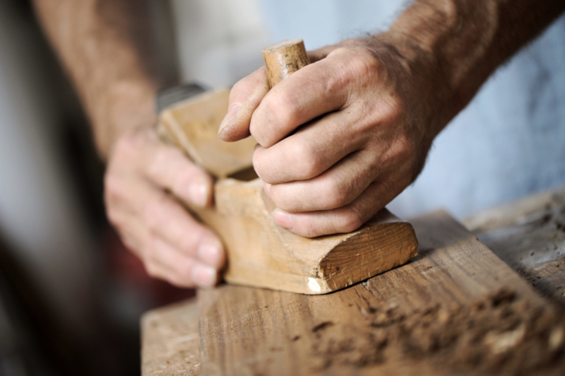 hands of a carpenter planing a plank of wood with a hand plane